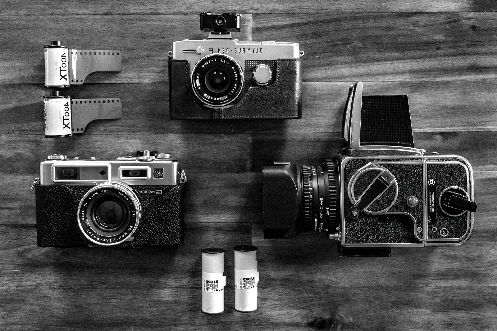 Three cameras sitting on a table: a Hasselblad 500CM medium format camera, an Olympus PEN FV half-frame camera and a Yashica Electro GSN 35 mm camera.